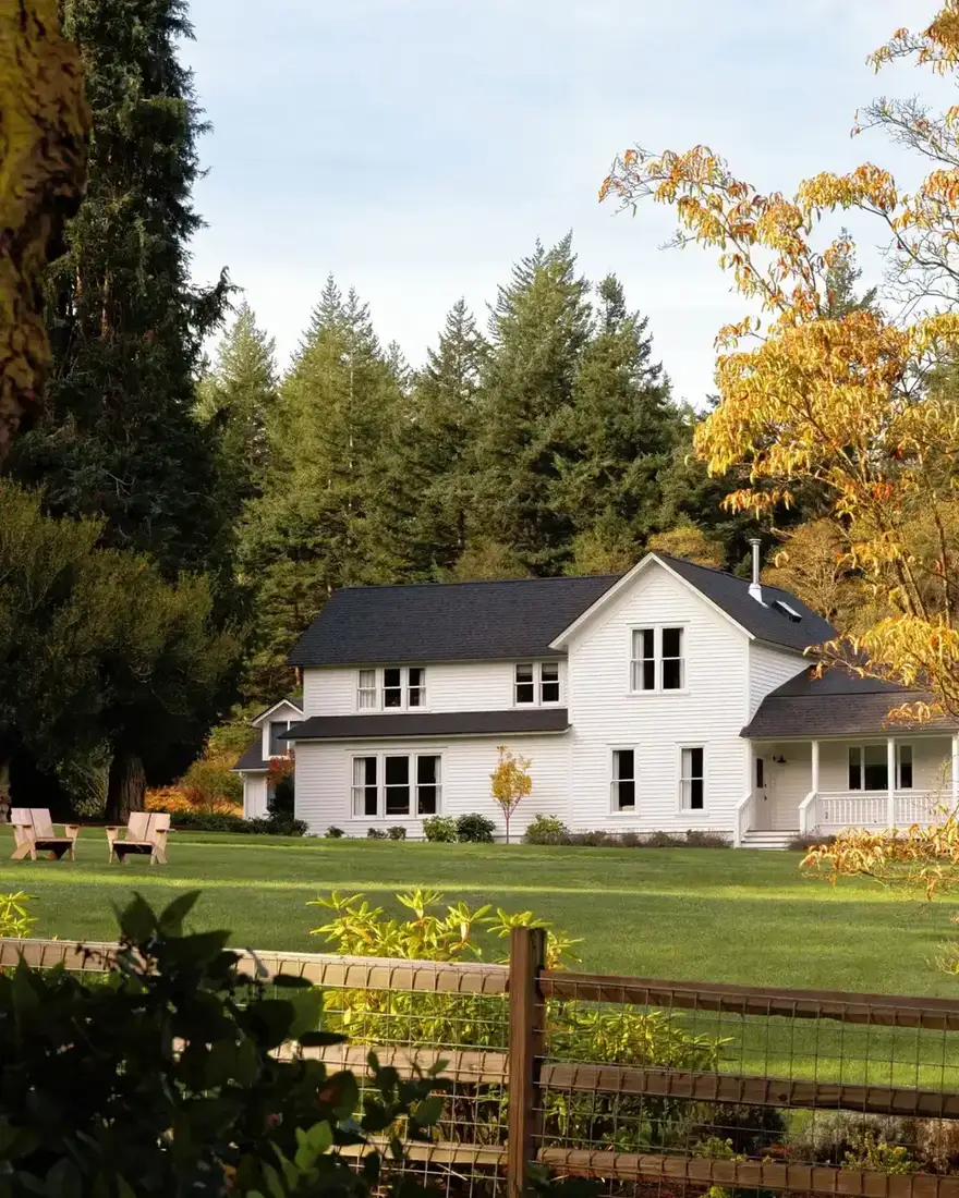 White farmhouse with black metal roof and post and rail fence in open meadow
