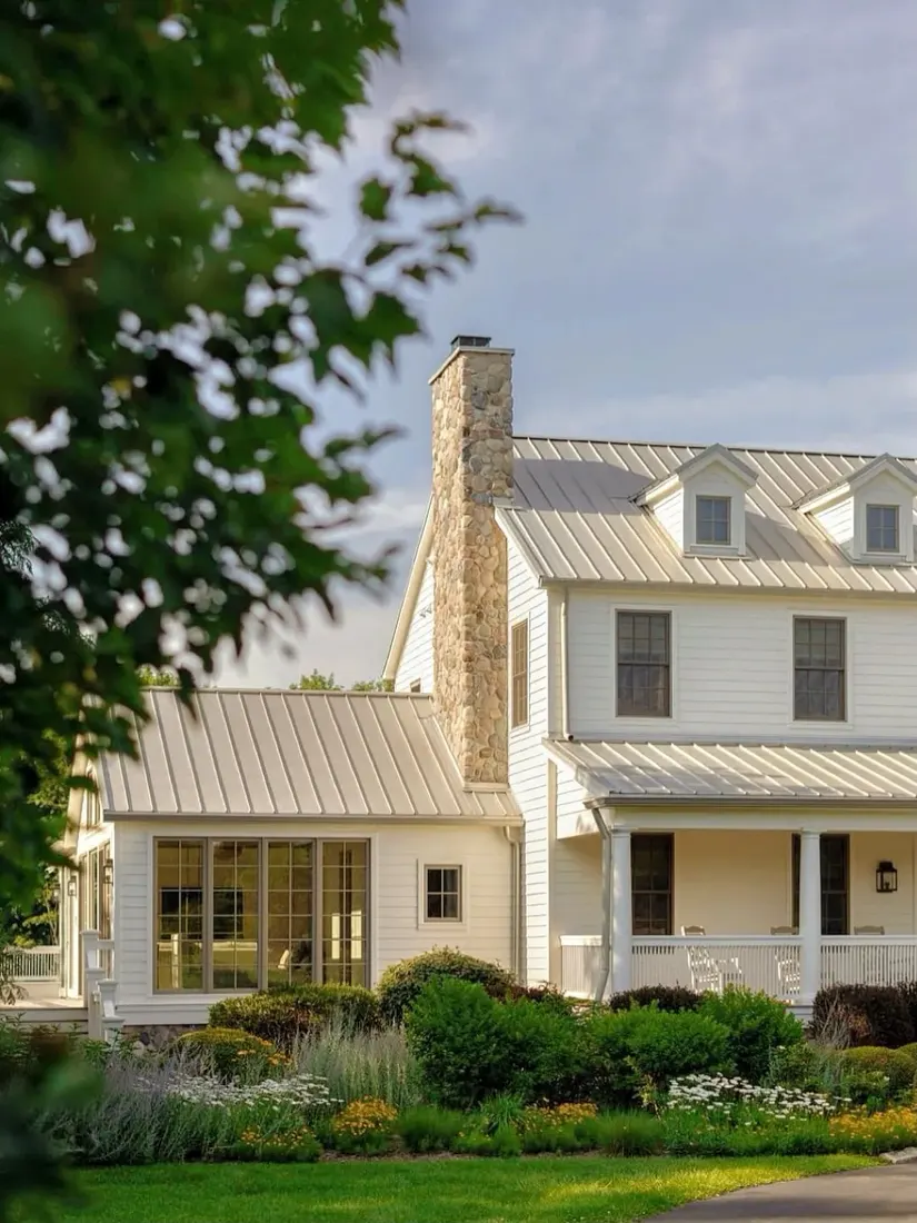 Cream farmhouse with a stone chimney and a dark standing seam metal roof