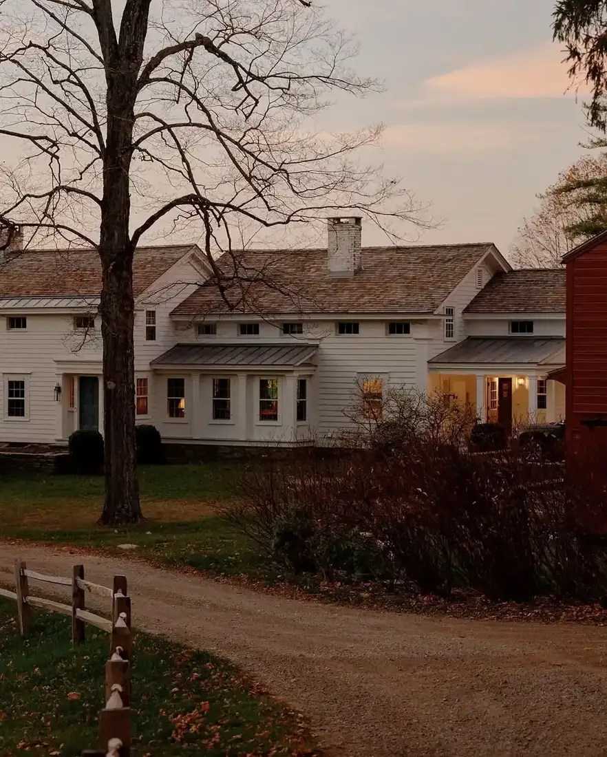 White clapboard farmhouse with a red barn further down a gravel lane