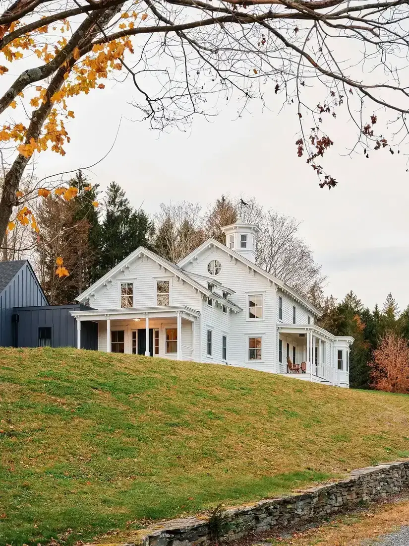 White farmhouse with a rooftop cupola set on a hillside behind a dry stone wall