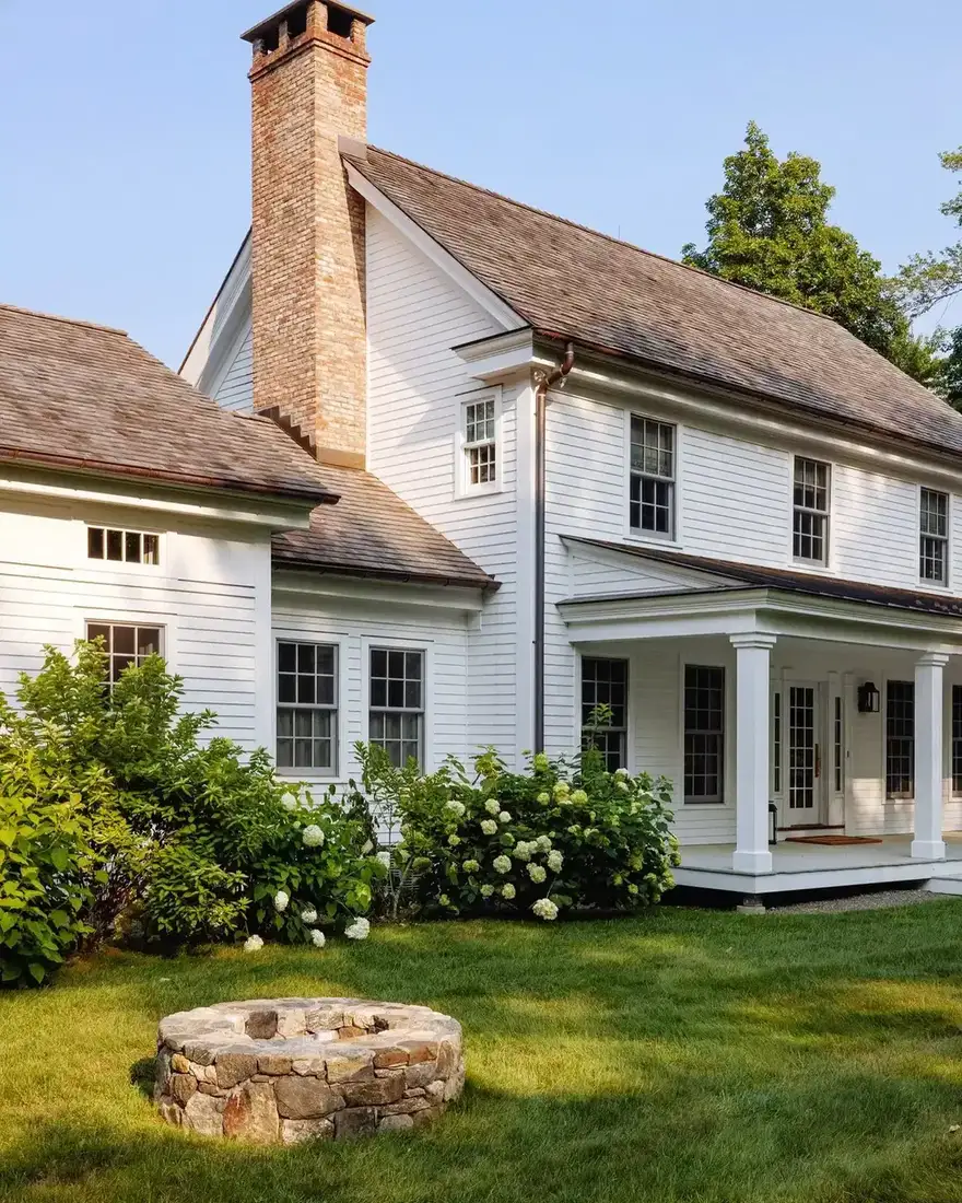 White farmhouse with front yard fire pit and warm white walls on a green lawn