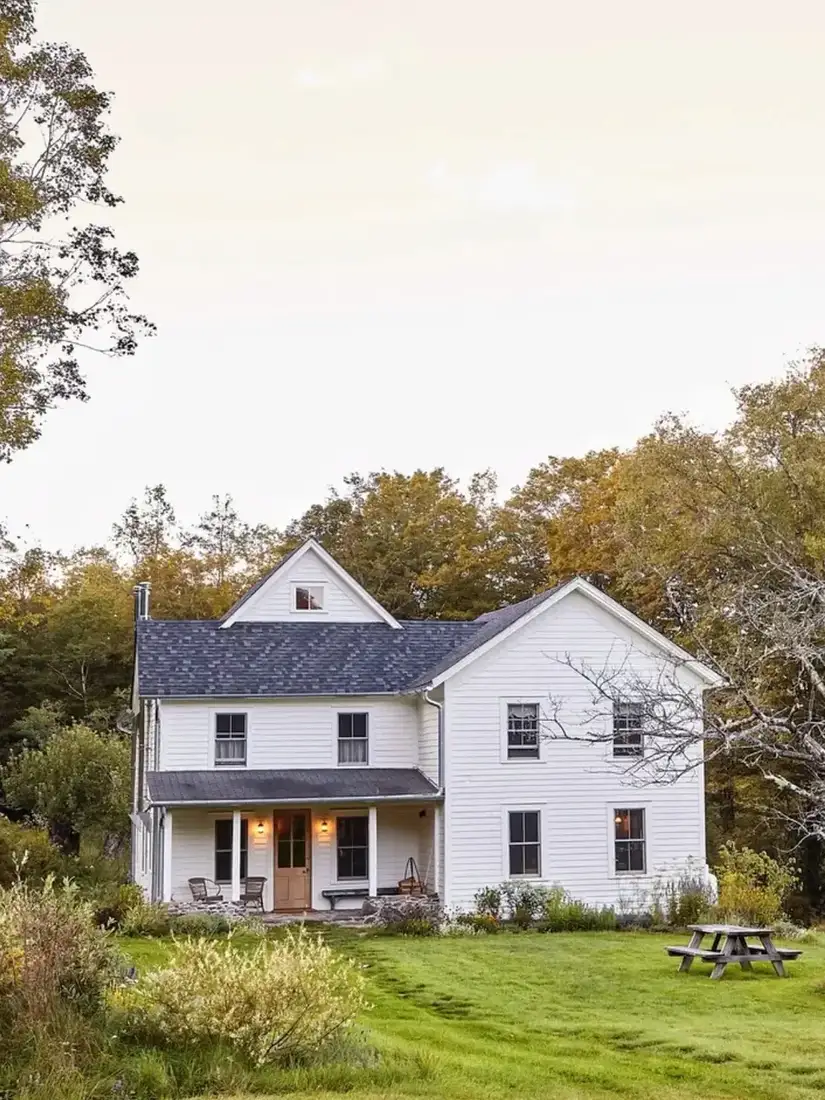 White farmhouse with soft grey roof set in open meadow with green fields