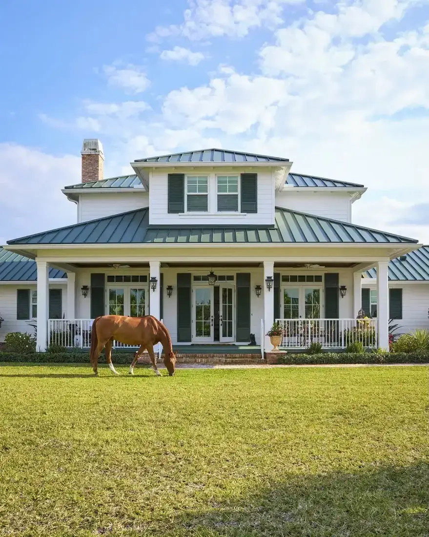 White farmhouse with green metal porch roof and white walls on a lawn