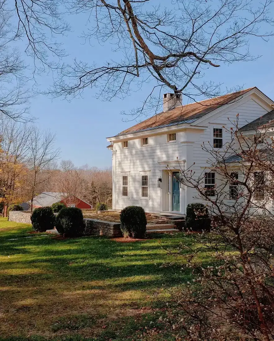 White farmhouse on hillside with bright blue door and clipped boxwood shrubs