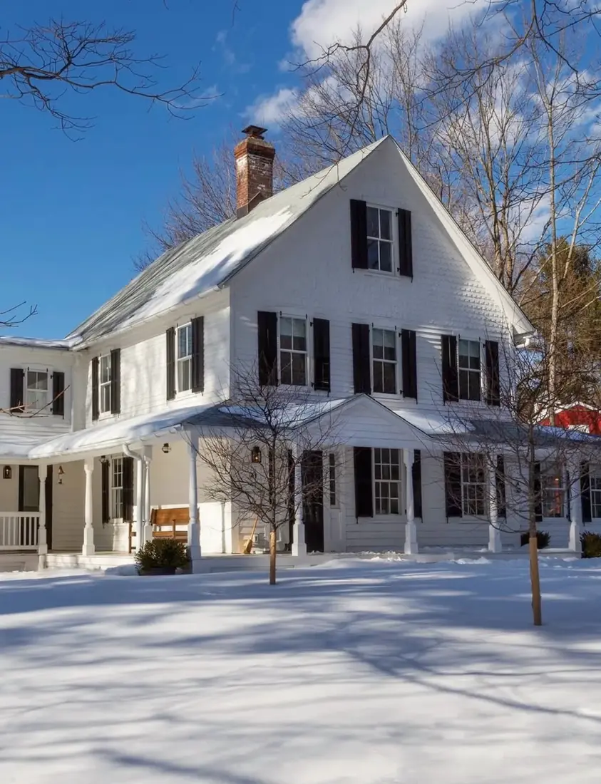White farmhouse exterior in winter snow with dark roof and warm white walls
