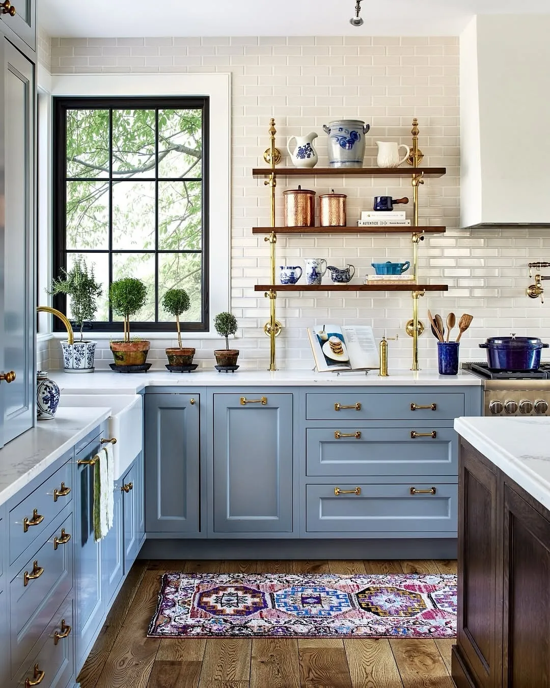 Blue kitchen cabinets with brass hardware and marble counters