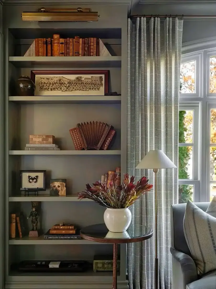Moody green built-in bookshelves in living room with plants and brass decor