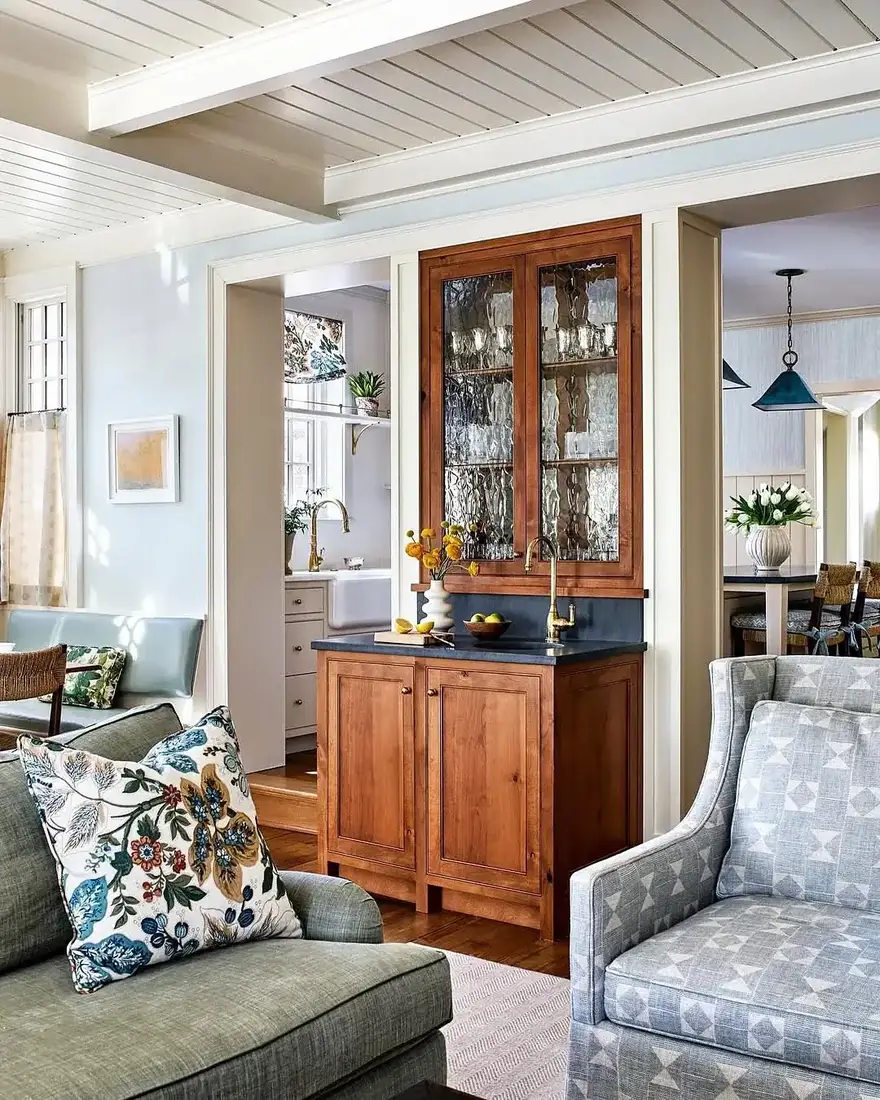 Lake house living room with antique wood hutch, soft textiles and warm light near windows