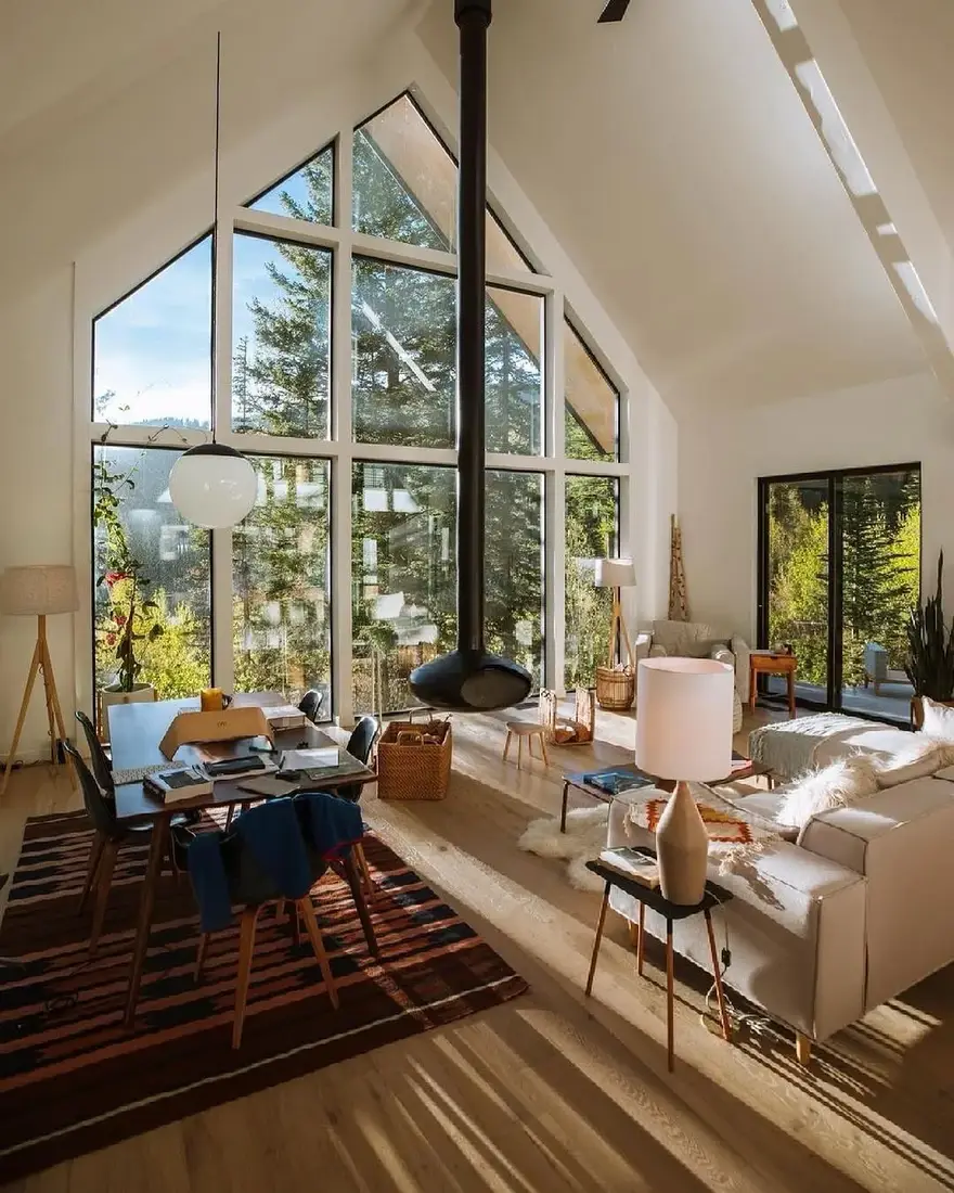 Modern A-frame cabin living room with tall windows, timber beams and soft textiles