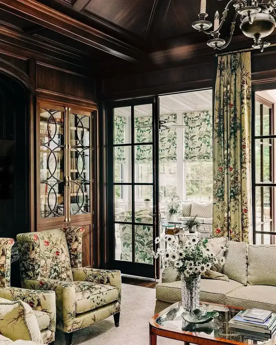 Dark wood paneled sunroom with floral chintz armchairs and curtains