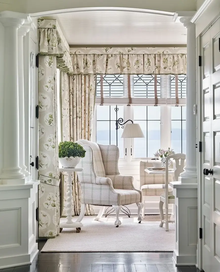 White sitting room with floral curtains and classic wing chair