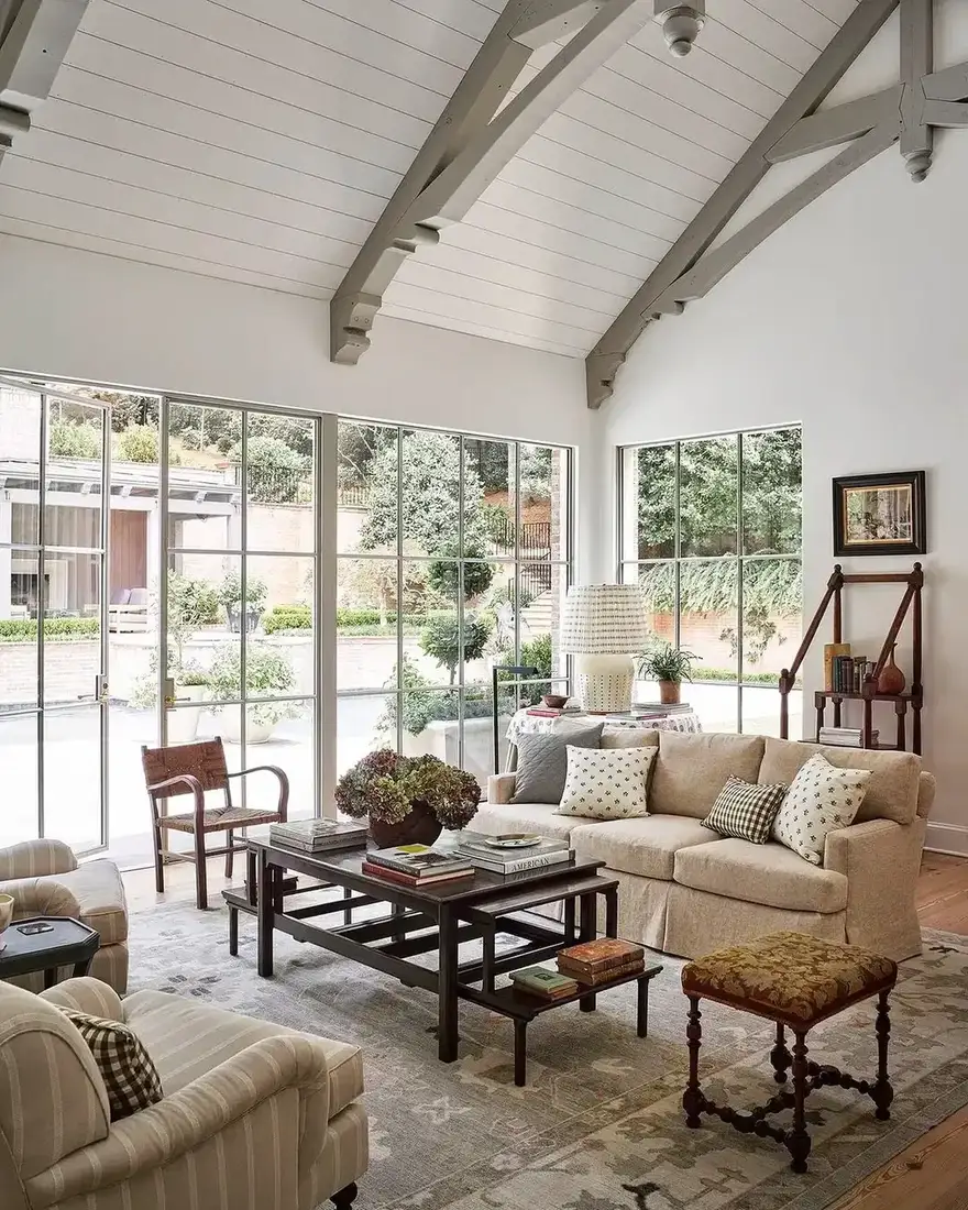 Vaulted sunroom living room with wall of windows and pale seating